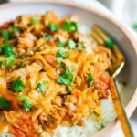 A serving of unstuffed cabbage roll bowl. Cabbage and turkey are mixed with a tomato sauce and served over rice. Gold fork is resting inside white ceramic bowl.