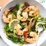 A bowl with zucchini noodles, asparagus and shrimp garnished with lemon and red pepper flakes.