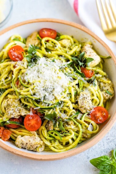 Ceramic bowl with pesto zucchini noodles with chicken and cherry tomatoes, topped with parmesan.