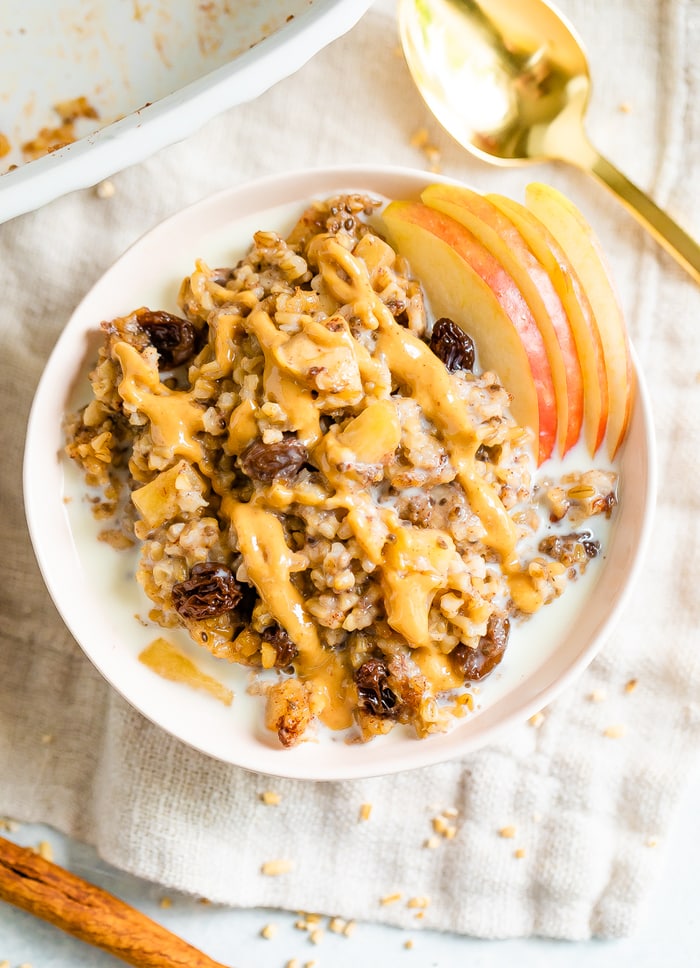 Overhead photo of baked apple steel cut oatmeal in a pink bowl with peanut butter drizzled on top.