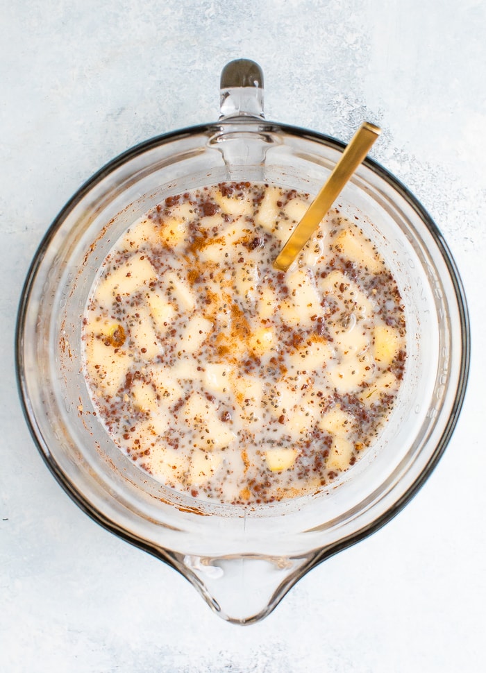 Ingredients for apple cinnamon baked steel cut oatmeal in a clear glass mixing bowl.