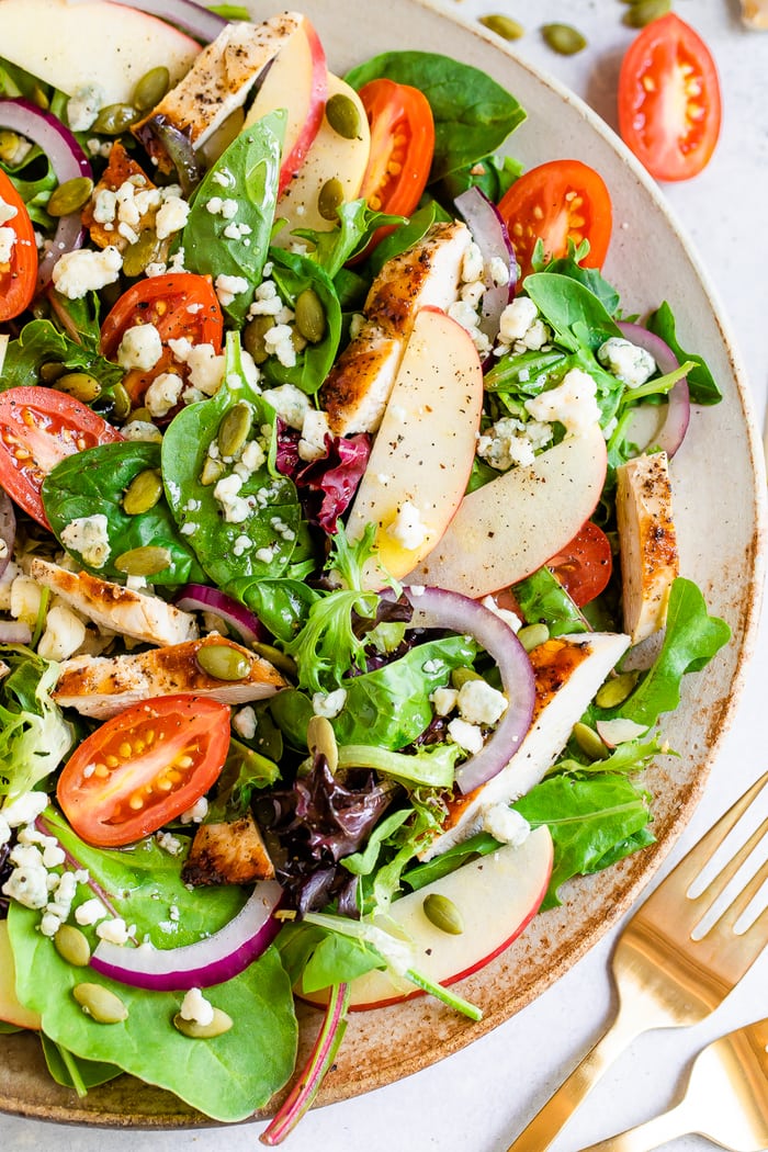 Fuji apple chicken salad with gorgonzola cheese, pepitas, cherry tomatoes and dressing on a large plate.