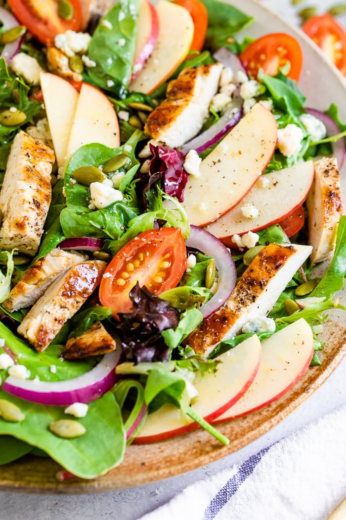 A serving of Fuji apple chicken salad with gorgonzola cheese, pepitas, cherry tomatoes and a dressing.