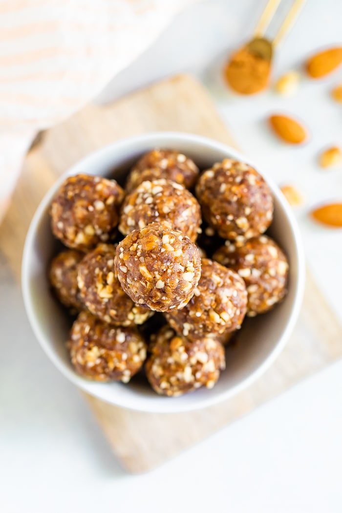 Pumpkin pie energy balls in a white bowl on top of a wooden cutting board.