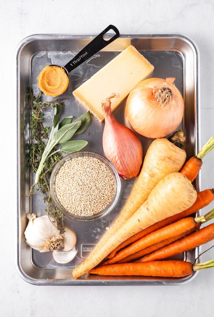 Tray with ingredients for carrot parsnip soup like onions, herbs, cheese, garlic and carrots and parsnips.