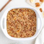 Maple pecan baked oatmeal in a white baking dish with bananas and pecans.