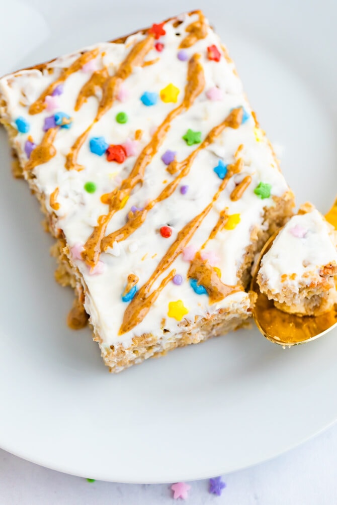 Slice of birthday cake baked oatmeal topped with frosting, nut butter drizzle and sprinkles.