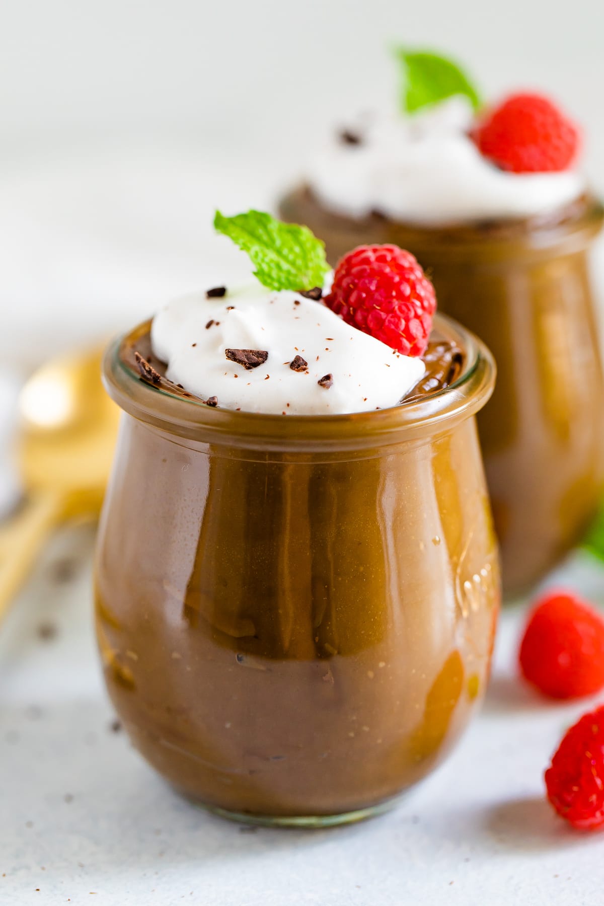 A serving of avocado chocolate pudding topped with whipped cream, a raspberry, and a fresh mint leaf.
