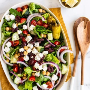 A large oval plate with a fresh Greek salad with cucumber, tomatoes, feta, olives, and lettuce.