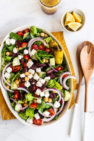 A large oval plate with a fresh Greek salad with cucumber, tomatoes, feta, olives, and lettuce.