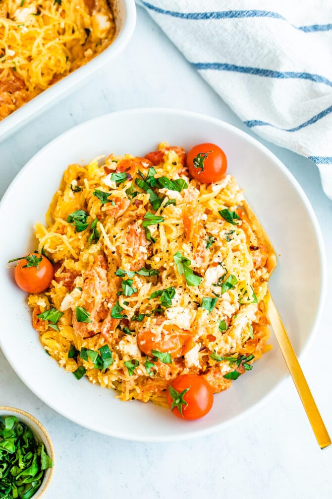 A serving of spaghetti squash with feta, basil and tomatoes in a bowl with a metal fork.