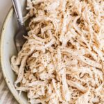 Shredded chicken in a large bowl with a metal fork.