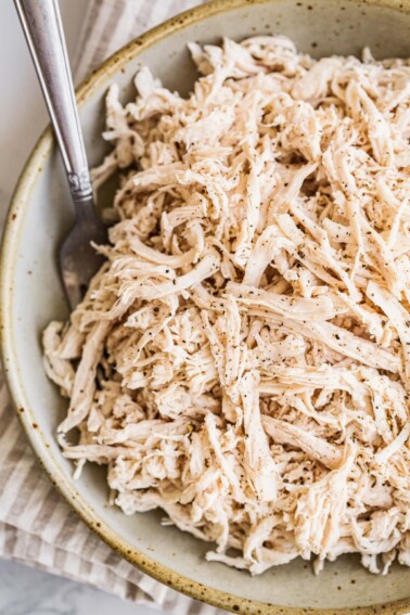 Shredded chicken in a large bowl with a metal fork.