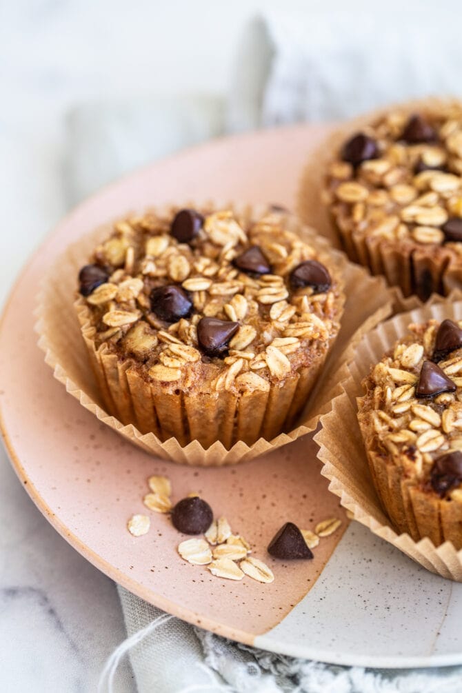 Three chocolate chip baked oatmeal cups on a plate, topped with chocolate chips.