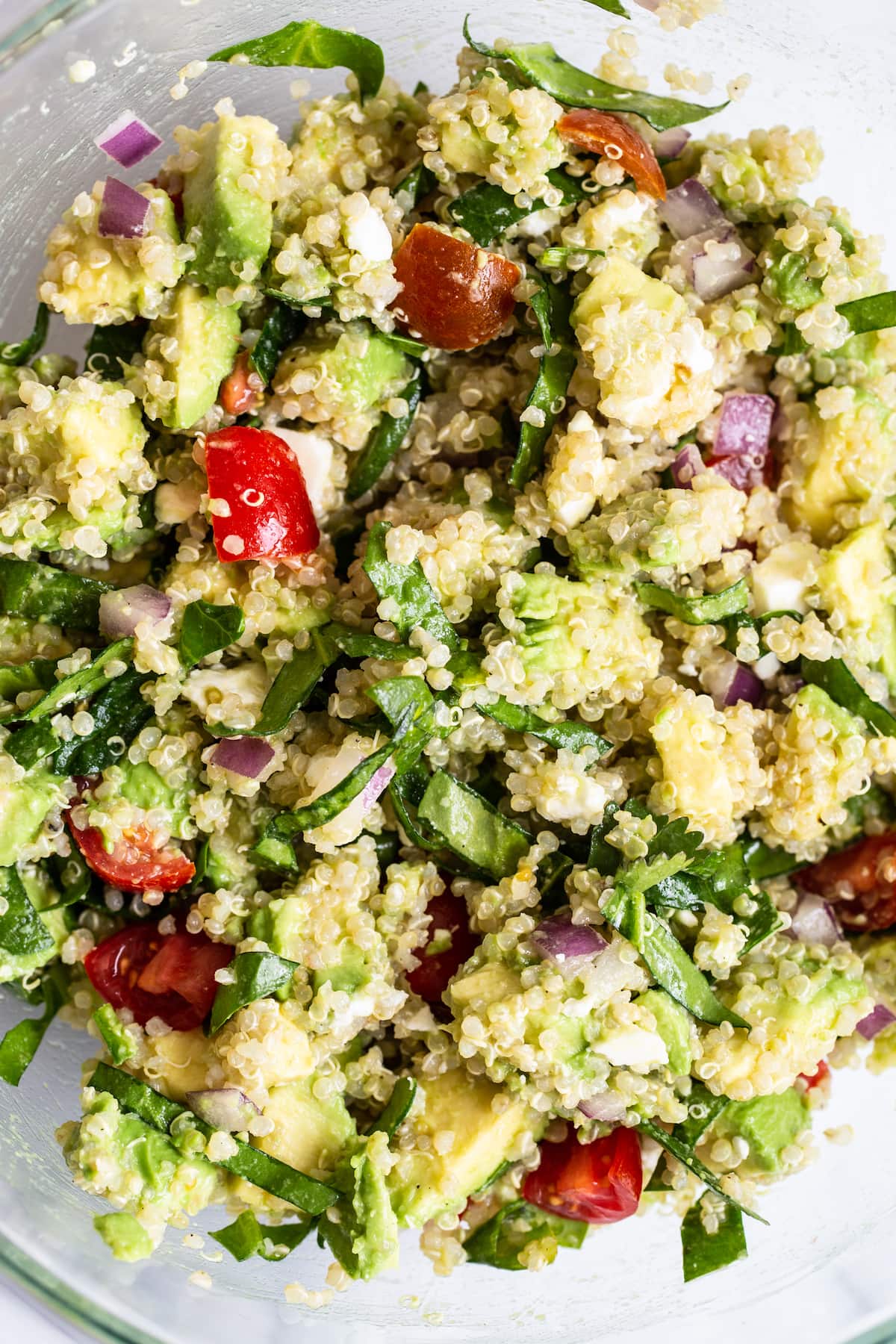 A serving of quinoa salad in a glass bowl with cherry tomatoes, red onion, feta cheese, and spinach.