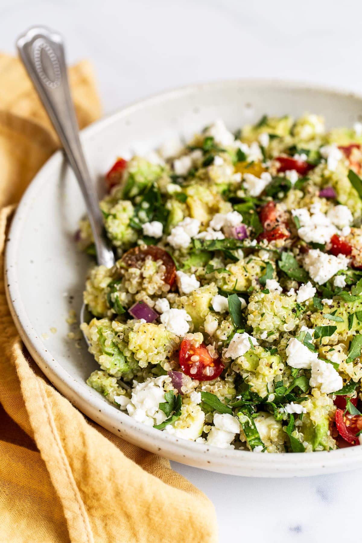 A large bowl of quinoa salad with feta cheese, cherry tomatoes, spinach, salt, and pepper.