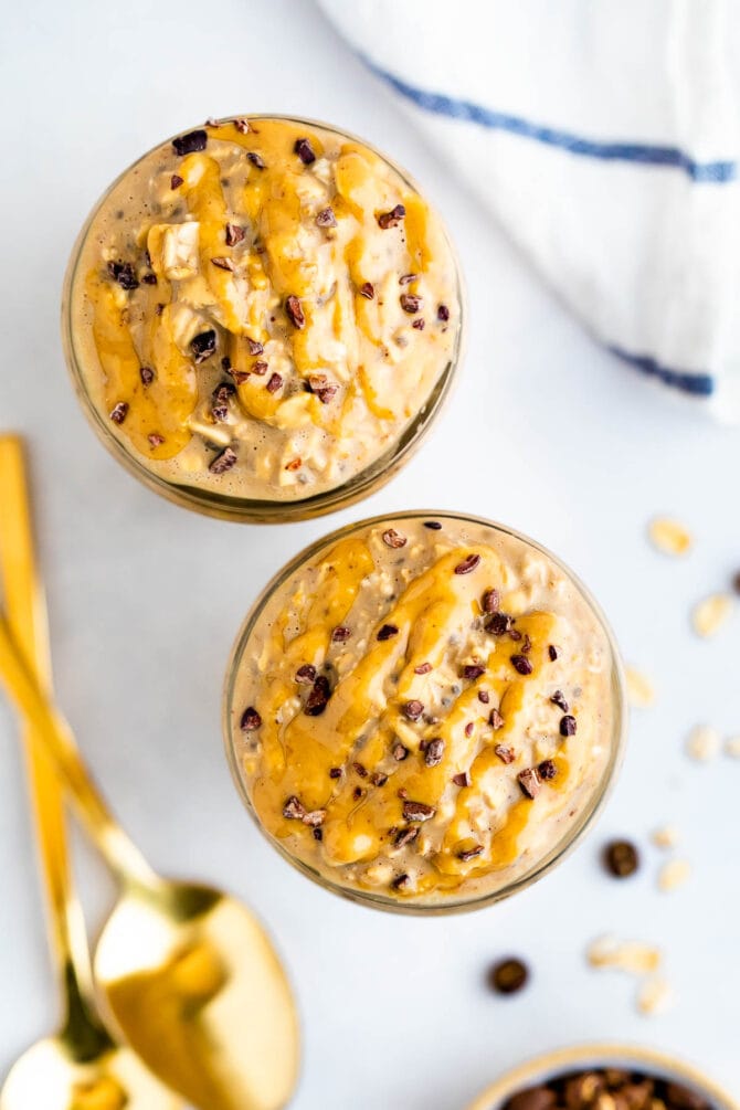 Two jars of coffee overnight oats topped with peanut butter and cocoa nibs.