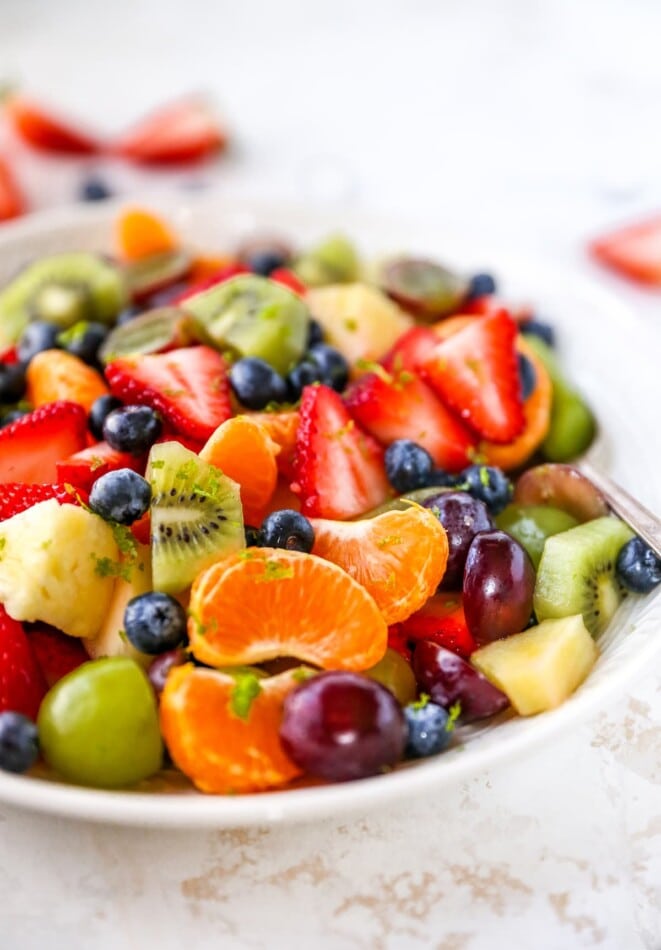 A bowl of fruit salad with clementines, kiwi, berries and grapes.