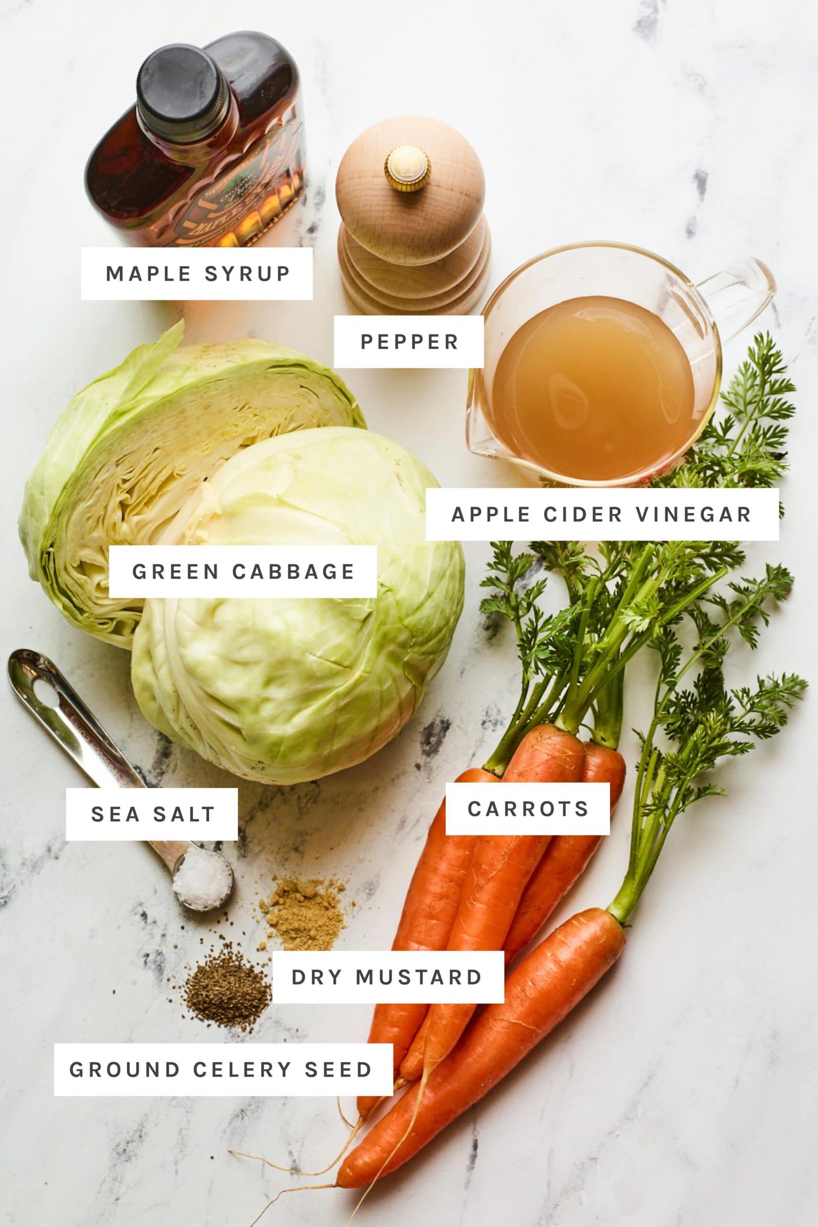 Ingredients to make vinegar coleslaw measured out on a table: cabbage, carrots, vinegar, maple syrup and spices.