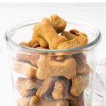Glass jar full of peanut butter dog treats in the shape of bones.