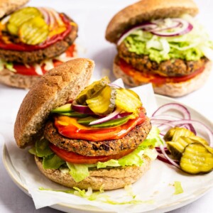 A black bean burger is served on a plate with two other black bean burgers in the background.