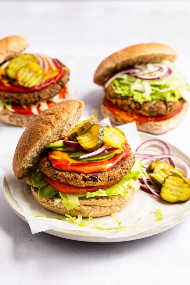 A black bean burger is served on a plate with two other black bean burgers in the background.