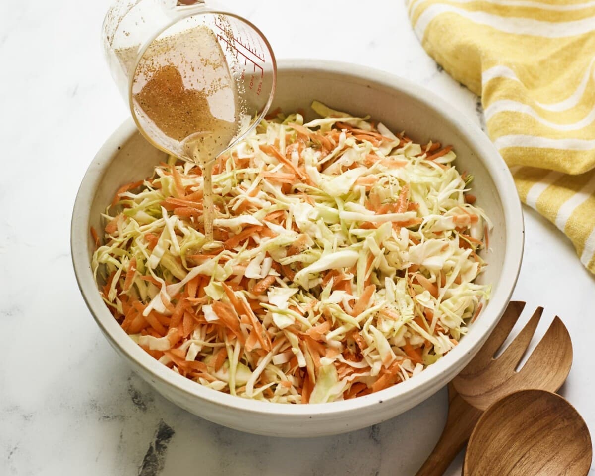 Pouring a vinegar dressing over a serving bowl of coleslaw.
