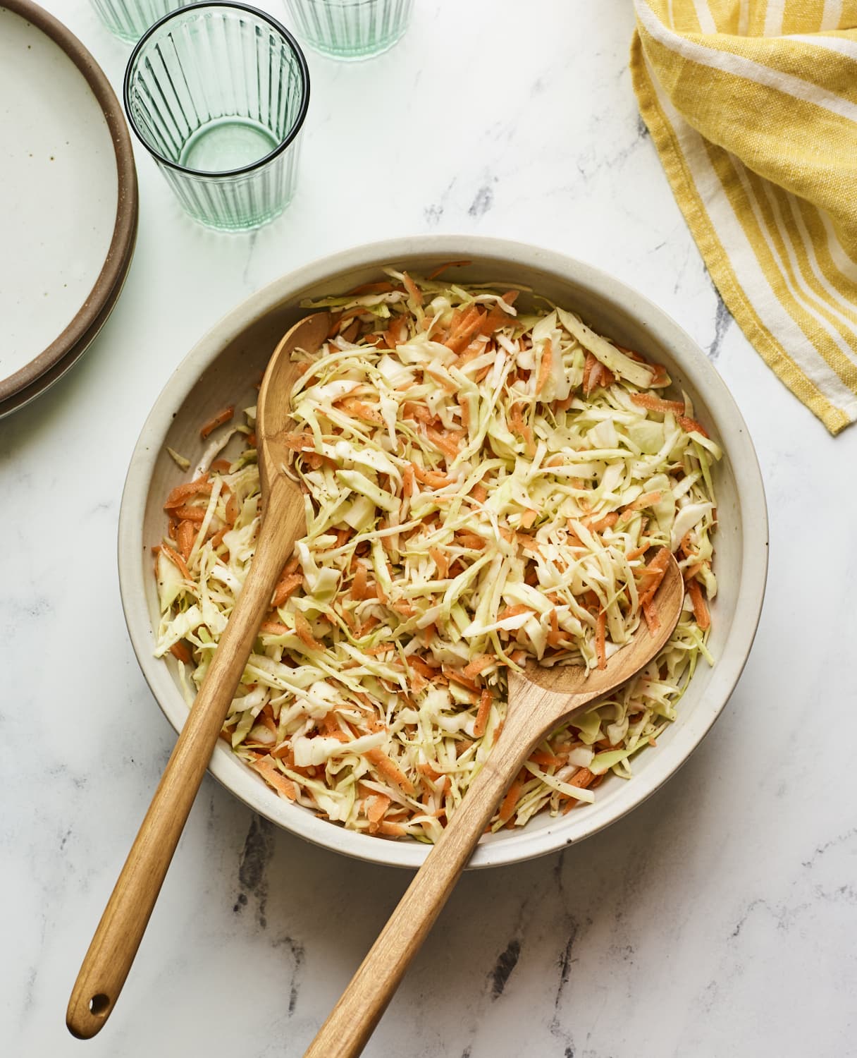 A large serving bowl of vinegar coleslaw with wood serving spoons.