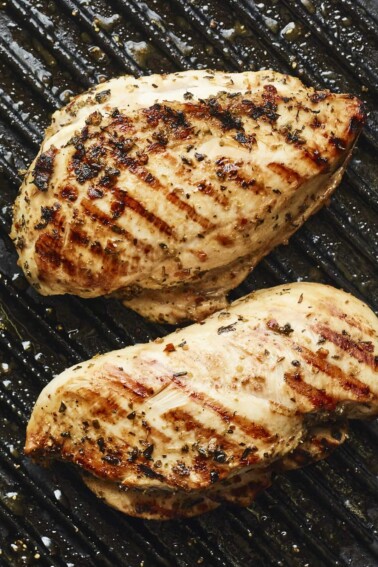 Two well-seasoned chicken breasts on a grill pan with grill marks