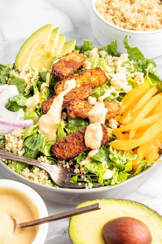 Blackened Tempeh Salad with Orange Tahini Dressing Salad topped with blackened tempeh, tahini dressing, peppers, onions, avocado and quinoa.