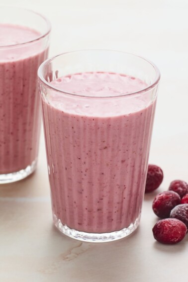 Two glasses of cranberry smoothie. Frozen cranberries are next to the glasses.