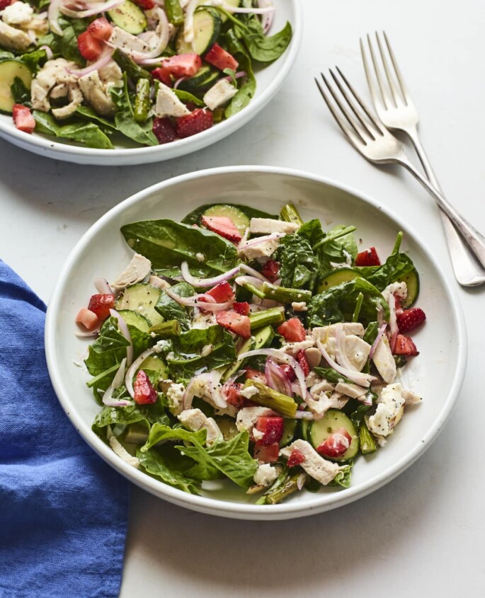 A serving of a spinach salad with chicken and strawberries in a large plate.
