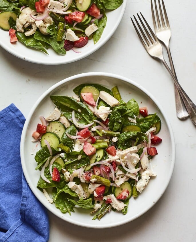 Strawberry Spinach Mason Jar Salad with Citrus Poppyseed Dressing Two plates of a spinach salad with cucumber, shredded chicken, strawberries, red onion, and asparagus.