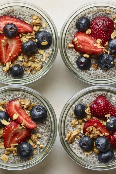 Four glass jars with chia pudding topped with fruit and granola.