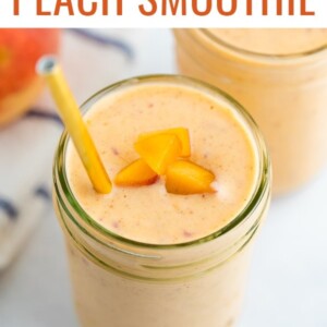 Mason jar with a peach smoothie garnished with a gold straw and peach pieces.