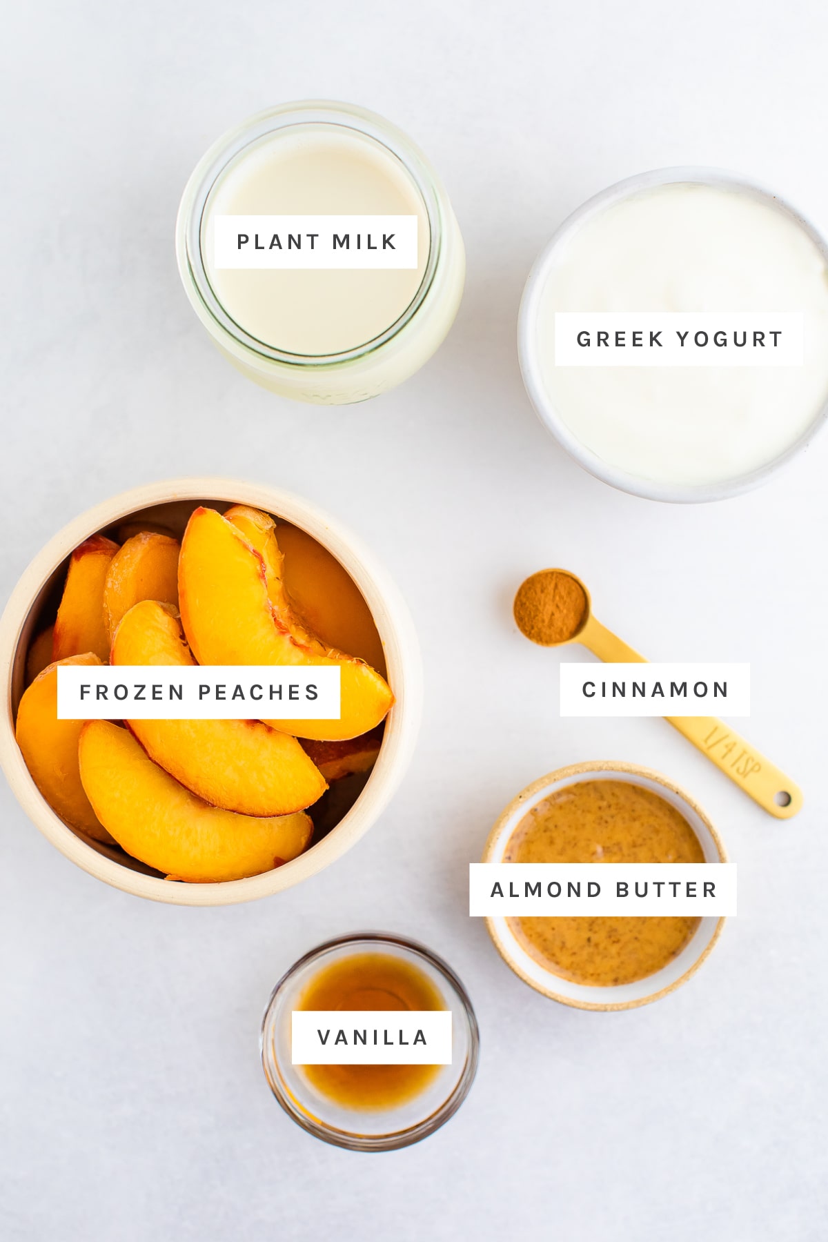 Ingredients measured out to make peach smoothies: plant milk, greek yogurt, frozen peaches, cinnamon, almond butter and vanilla.