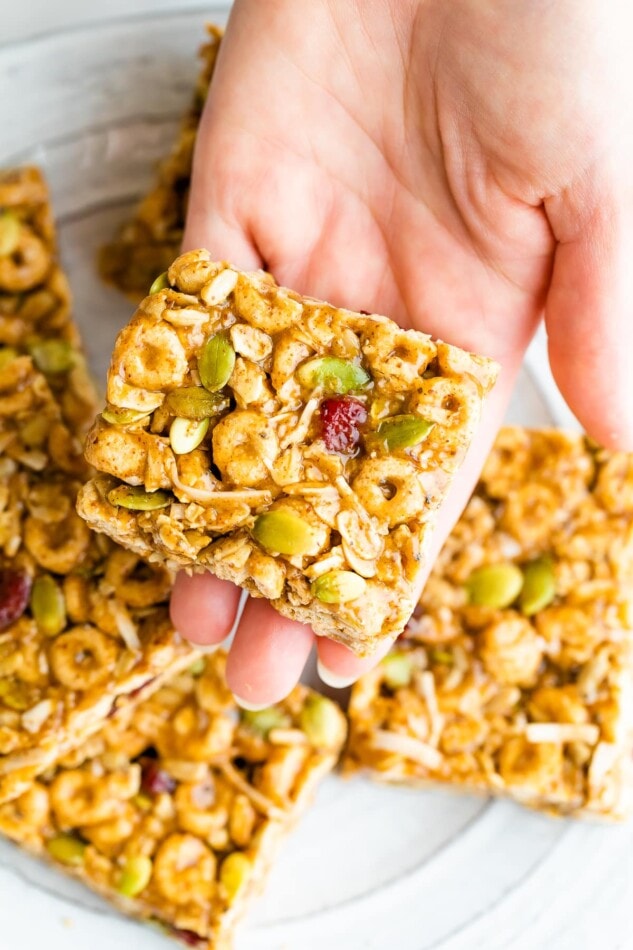 Superfood Cereal Squares -- Like trail mix in bar form, these cereal squares are packed with nutrient dense superfood seeds, whole grain cereal and dried fruit. They’re held together with a blend of almond butter and honey so they’re nutty, sweet and perfectly chewy with a little crunch from the cereal. Hand holding a cereal bar.