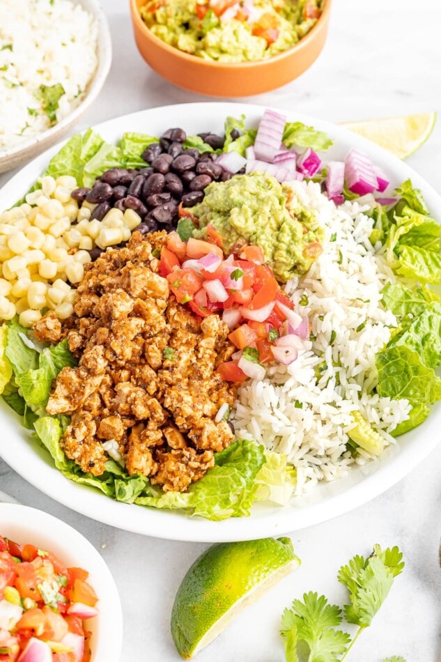 A serving of a burrito bowl with sofritas, black beans, corn, lettuce, guacamole, red onion, and white rice.