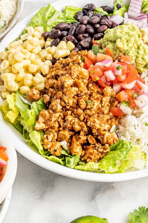 A large bowl with sofritas, black beans, corn, lettuce, avocado, and rice.