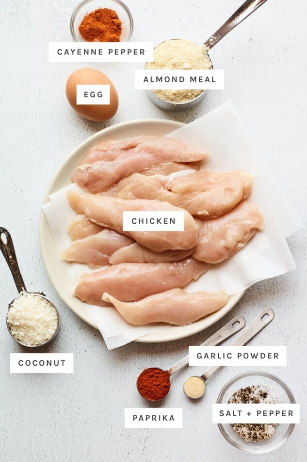 Pin this image to save this delish Baked Paleo Chicken Tender recipe for later! Ingredients measured out to make baked chicken tenders: cayenne pepper, almond meal, egg, chicken, coconut flakes, garlic powder, paprika, salt and pepper.