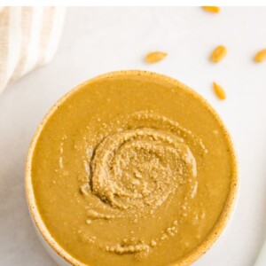 Overhead shot of sunflower butter in an open container with a spoon and some sunflower seeds scattered around.