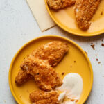 Two plates with baked chicken tenders being served with a ranch dipping sauce.