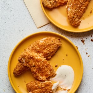 Two plates with baked chicken tenders being served with a ranch dipping sauce.