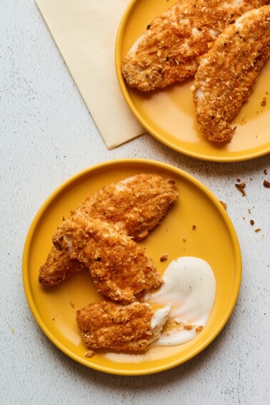 Two plates with baked chicken tenders being served with a ranch dipping sauce.