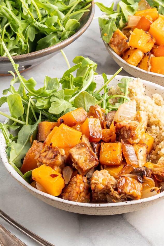 This tempeh butternut squash bake is loaded with protein, veggies and flavor! It's easy to make, vegan, gluten-free and absolutely delicious! A shallow bowl filled with butternut squash tempeh bake served with brown rice and greens.