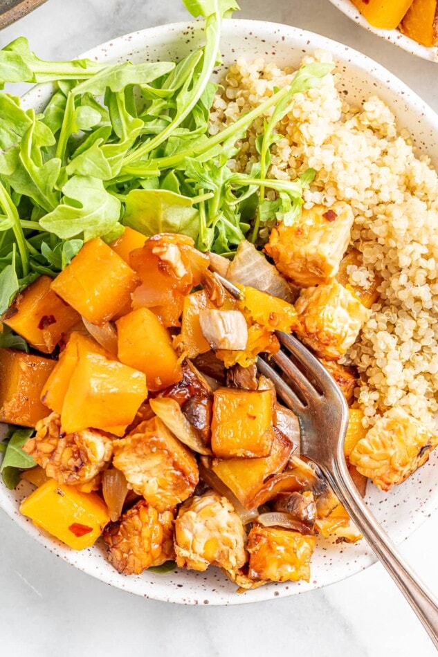 One Pan Tempeh Butternut Squash Bake that's loaded with protein #vegan #glutenfree Overhead view of butternut squash tempeh bake served with brown rice and greens, a fork is scooping a bite.