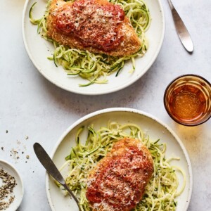 Two plates being served with chicken parmesan over zucchini noodles.
