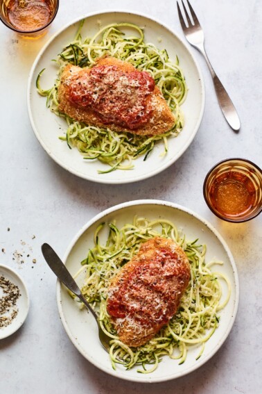 Two plates being served with chicken parmesan over zucchini noodles.