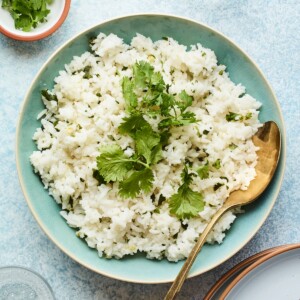 A serving of cilantro white rice topped with extra fresh cilantro leaves and a metal spoon to the side.