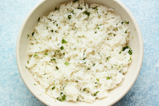 A bowl of white rice with chopped cilantro, lime zest, and lime juice.
